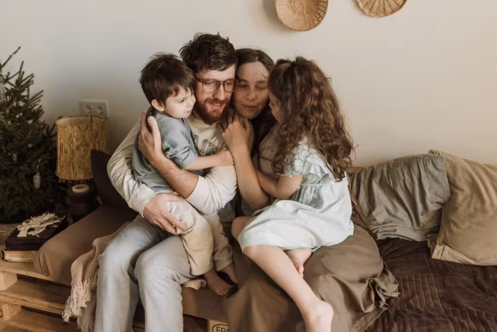 Familia con dos hijos abrazados en casa en ambiente cálido — reflexión sobre el papel de la familia en el hogar