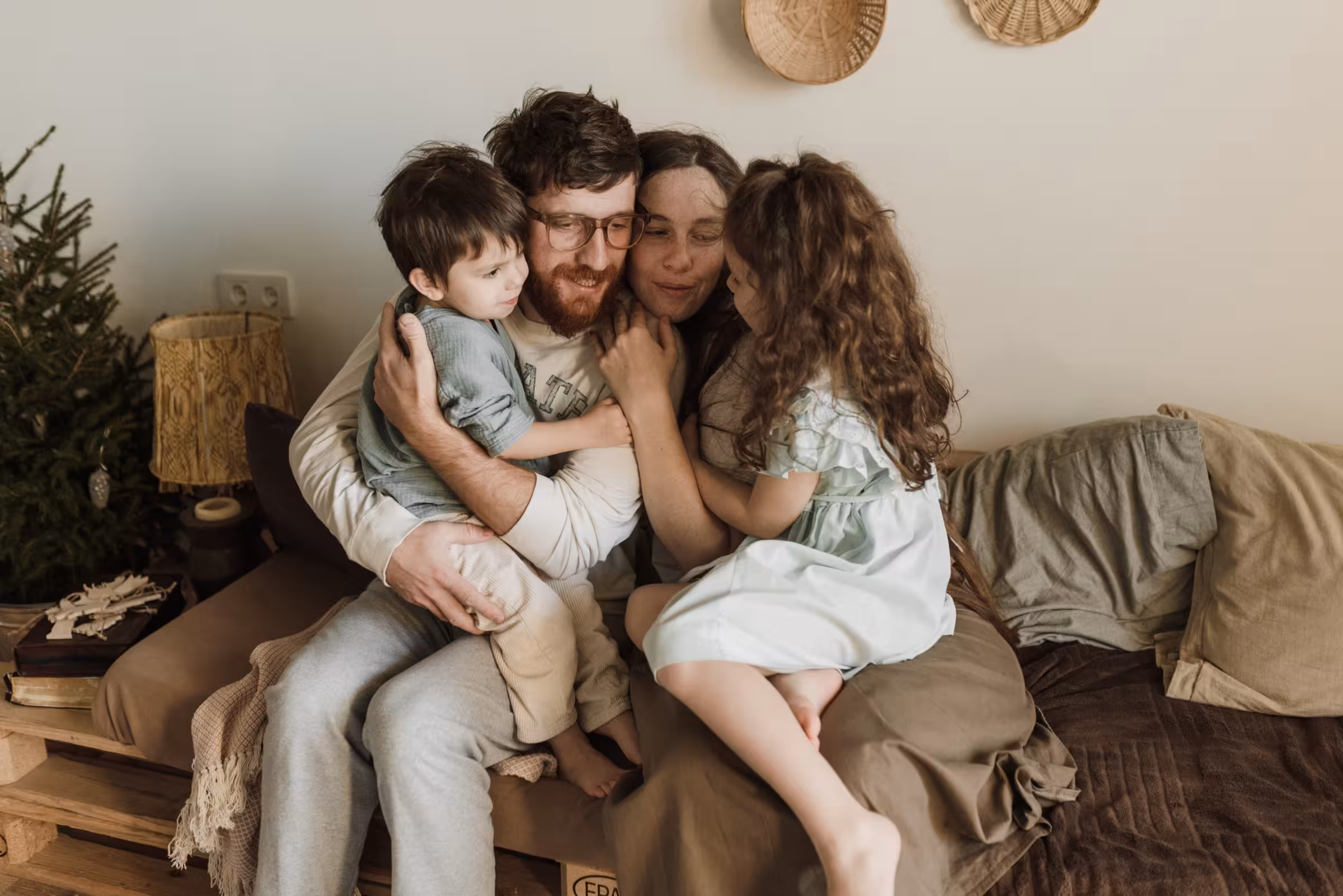 Familia con dos hijos abrazados en casa en ambiente cálido — reflexión sobre el papel de la familia en el hogar