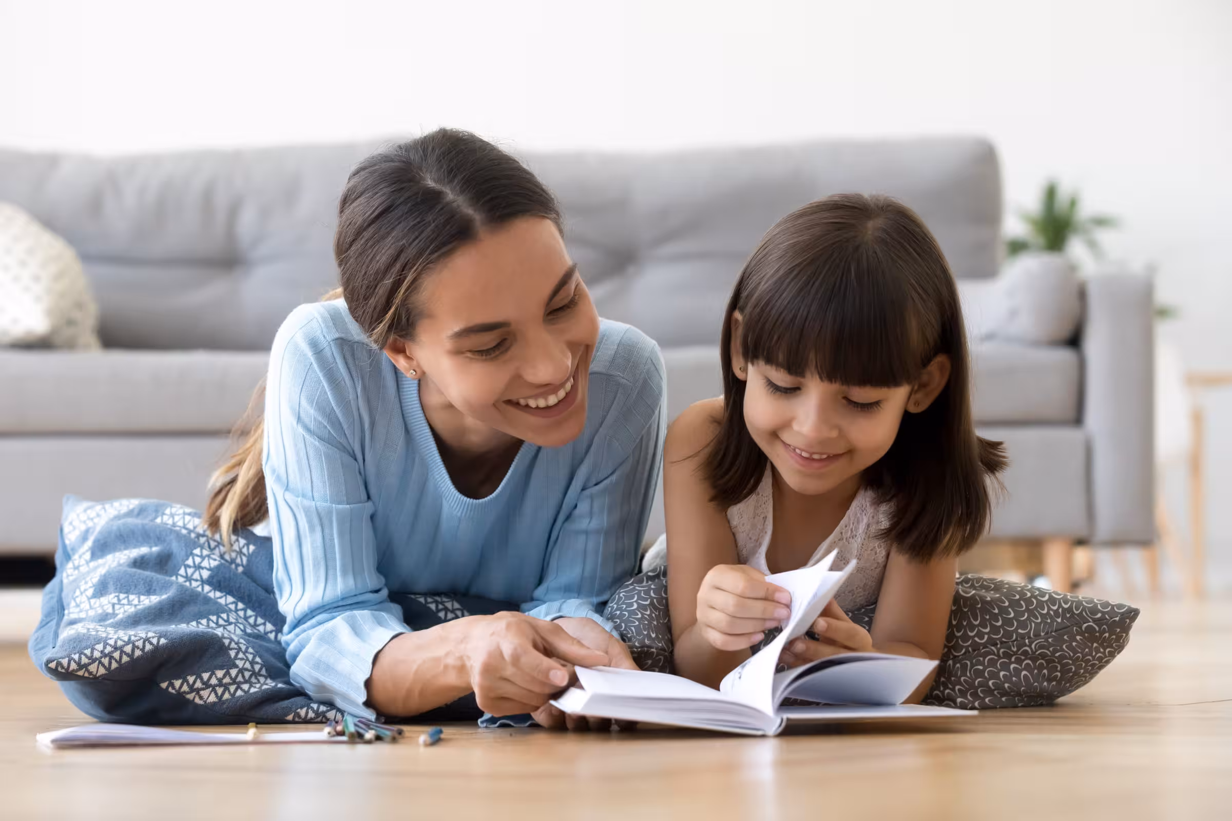 Caring mother reading book with little kid girl at home