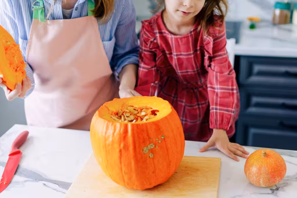 Feliz familia, madre y niño, niña feliz está cortando una calabaza y se está preparando para la fiesta de Halloween. Feliz Halloween. Receta de puré de calabaza. Ingredientes para pastel de calabaza para el día de Acción de Gracias.