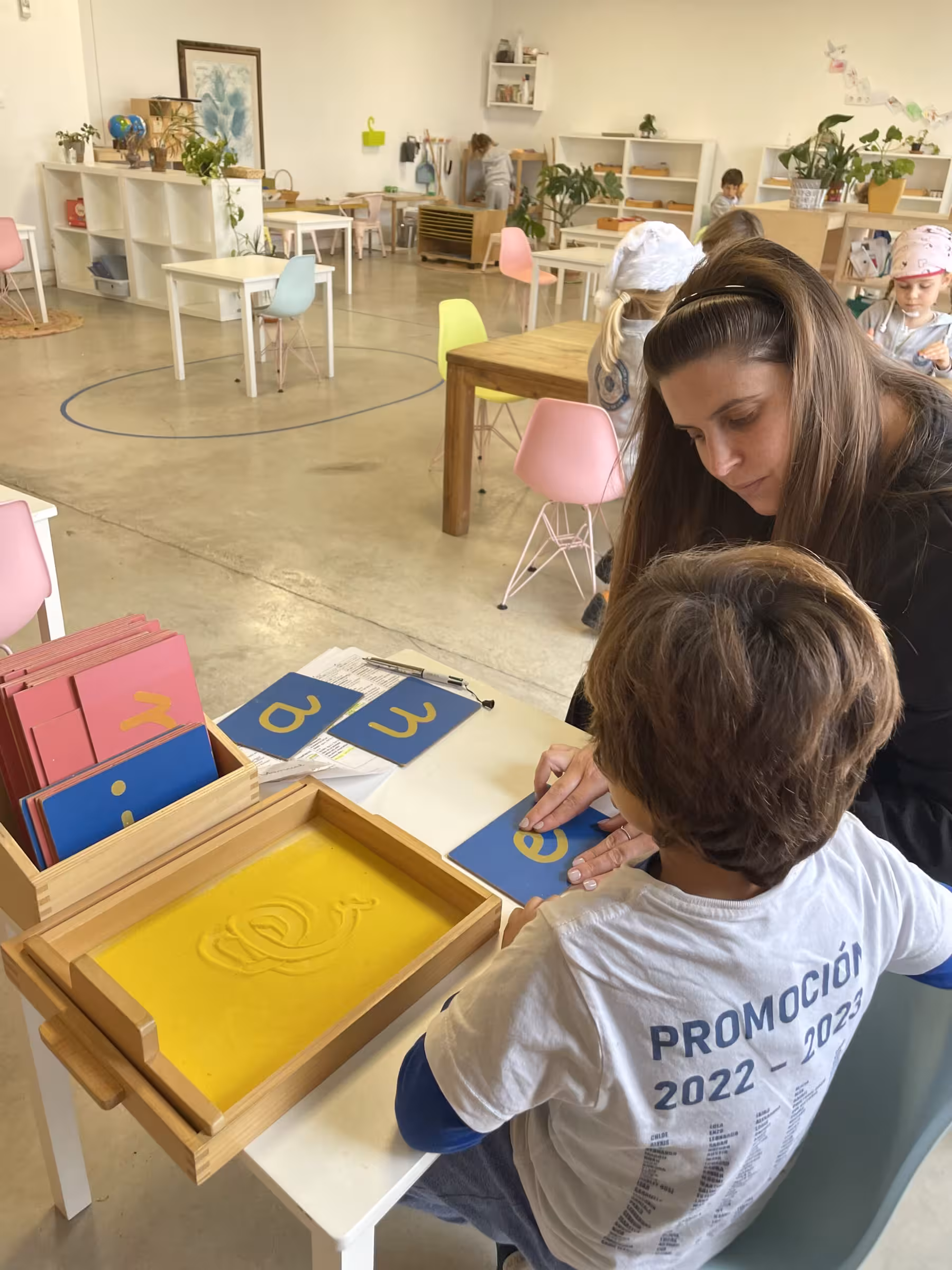 Profesora del IMS Sotogrande trabajando con alumno en bandeja de arena y letras Montessori — promoción 2022-2023