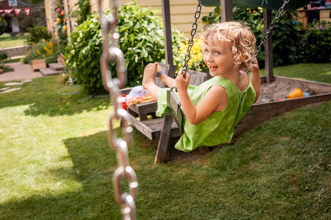 A young girl smiles while swinging on a porch swing.