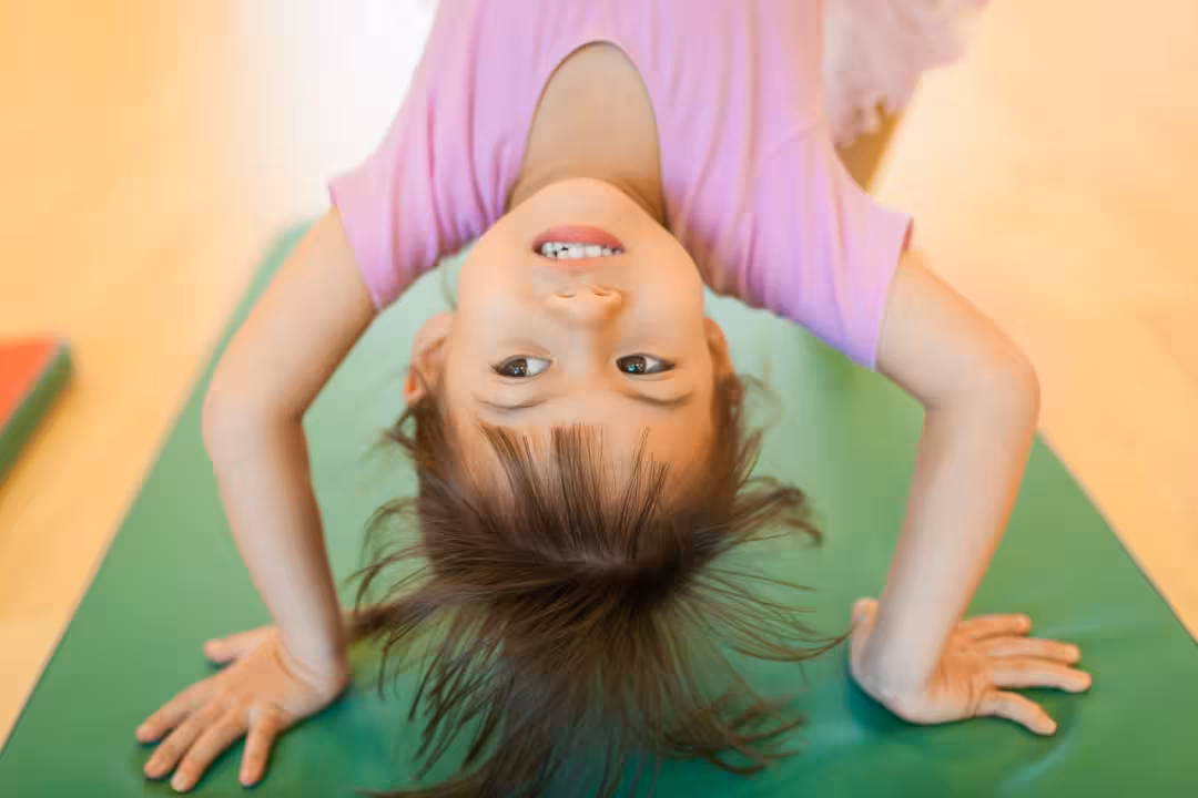 A young girl smiling upside down on a green mat.