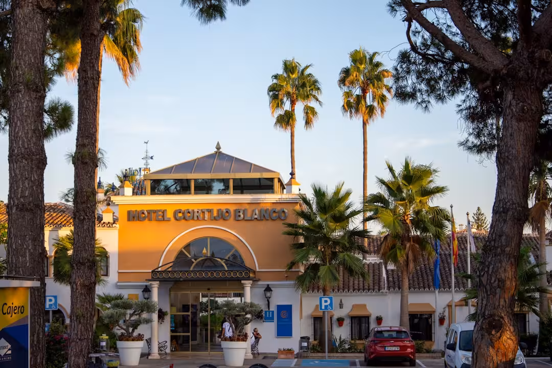 Hotel cortijo blanco building framed by palm trees at sunset.