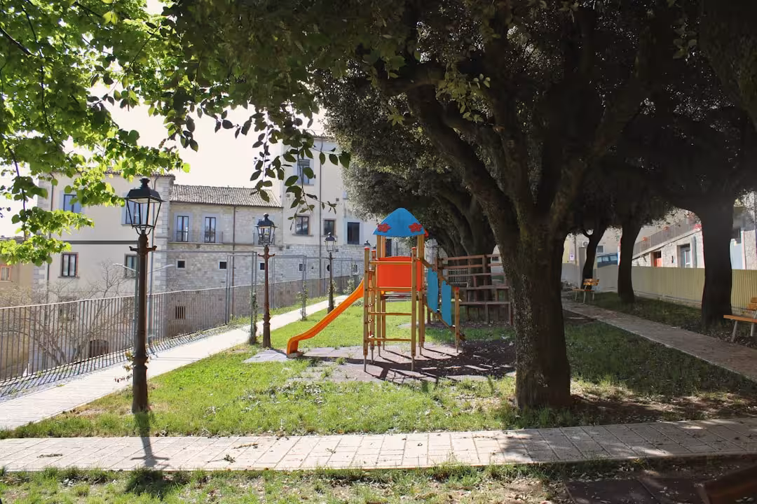 Playground equipment in a park with trees and buildings.