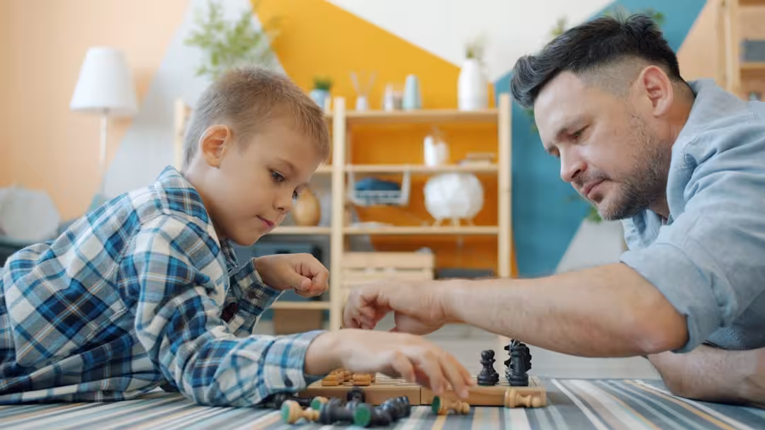Father and son playing chess on the floor.