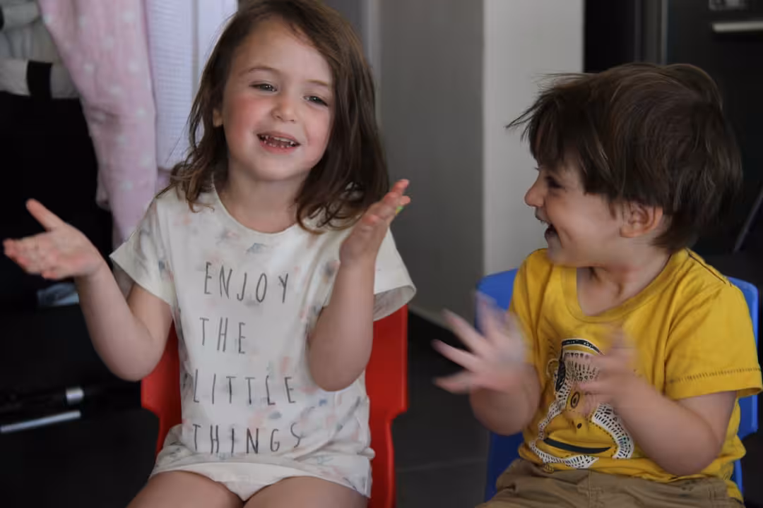 two young children sitting in chairs with their hands in the air